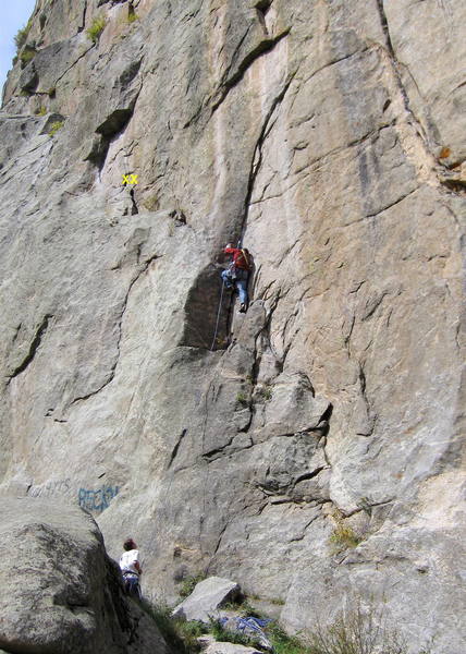 Climber starting the crux section of the first pitch. There is a 2-bolt anchor on the ledge to the climber's left.