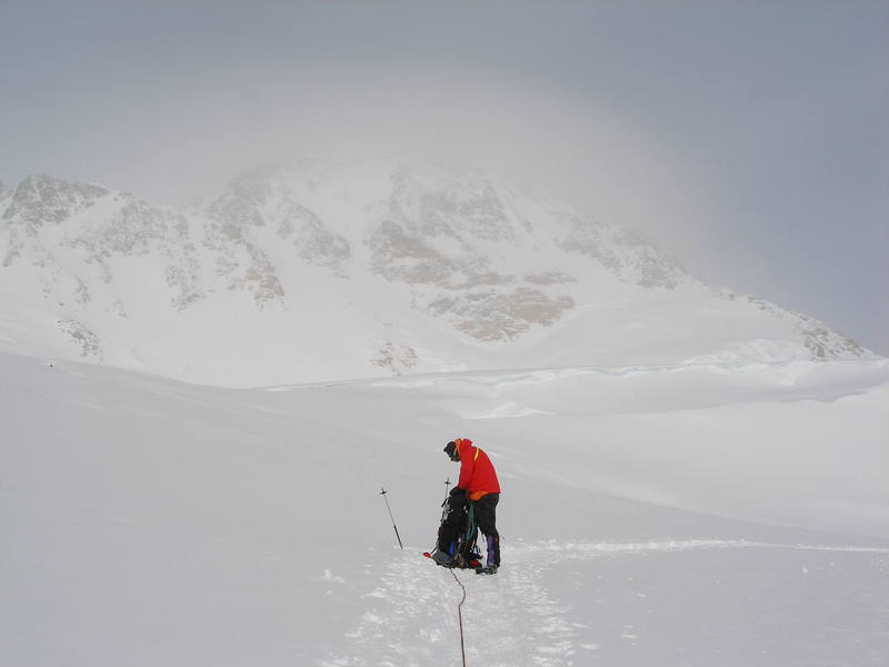 The Belly of the Beast: The west face of Denali, viewed from about 13,700 feet. The large camp at 14,000 feet is just out of sight, on top of the plateau that cuts across the middle of this photo. From this point you can see the West Buttress (ascend to the top of the Buttress via a slope & couloir just left of center), the Messner Couloir (just left of the large expanse of rock at center) and the Orient Express (right of center) on the west face of Denali. High camps on the West Rib are in the center of the skyline on the right, and the West Rib ascends the upper slopes of the Orient Express. The fuzz on top of the mountain is a giant cloud of wind blown snow, which suggests that it would be a really, really bad idea to go for the summit on this day.