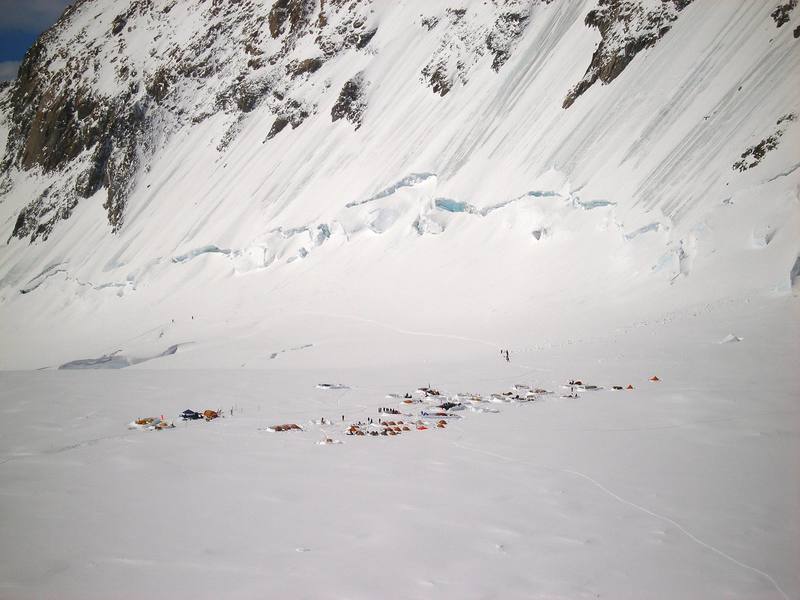 The West Buttress camp at 14,000 feet, viewed from a point below the Orient Express, on the way up the West Rib cutoff. The tents on the left side of the camp are staffed by the National Park Service, and typically include a rustic medical facility. The ascent to this camp is via the boot track that is visible beyond the camp. There are ice climbs on the steep ground above the boot track, on the flank of the West Buttress. The West Buttress route ascends fixed lines on a slope that is just out of the photo, on the right.
