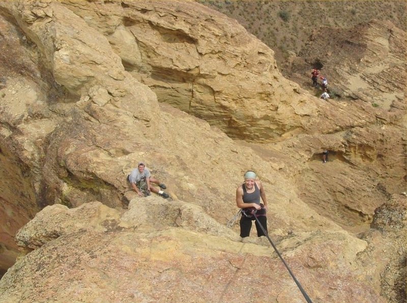 Carrie rapping from the summit of Brogan Spire with Mark waiting at the optional 2nd pitch belay (anchor requires gear). Further below a climber is exiting the western opening of the cave while another group of climbers are near the first pitch anchors (2 bolts).