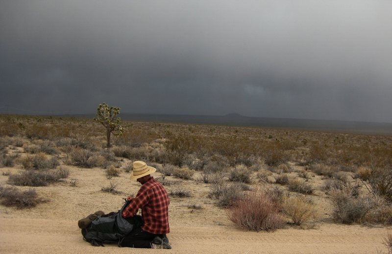 Jonny putting on rain gear as we left Marl Springs on the old historic Mojave Road. Note the stormy sky over the Cima Dome in the distance. <br>
<br>
After brushing up on a few history books, and reading some of first travelers/explorers, and native peoples personal accounts, and experiences in the east Mojave desert; it's fun to imagine how the ancient tribes, the Mojaves, Chemehuevis, Spanish Conquistadors, Jedidiah Smith, and all the other brave, and adventurous souls who lived in, or entered this land fared.<br>
<br>
We were fortunate to get a little break from the rain after being cooped up in our bivy sacks for a good part of the day at Marl Springs. We took advantage of it, and took a side hike to locate some old mines; it was worth it, as we came across some fairly untouched old mining ruins in a beautiful area; but the break in stormy weather was short-lived, as we watched another storm moving in. In this photo we had 9 miles of hiking left in stormy weather on our Mojave Road adventure. We felt lucky to not see another soul during our trek, and didn't mind hiking in the rain, and wind.<br>
<br>
1/13/10