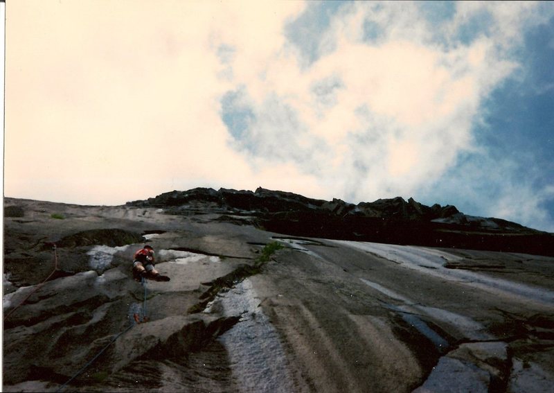 Scanned photo of myself getting past the crux on aid. The route goes up the expanding arches above the dike near to me.