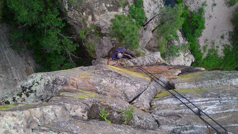 Arjun cleaning on rap. Drops into the ledge below. The route goes to my left down a slope to the chimney. Rap the tree.