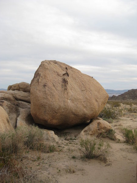 Stand on the smaller rock and reach up to the black hold, the put your foot up there too.