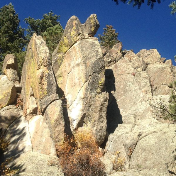 Overhanging Face (5.12?) is on the left face of the leftmost fin. Overhanging Left-Leaning Arete (11a) lies on the front of the leftmost fin. Ear Rings (10a) climbs the left edge of the east face of the middle fin, which has ears on top. Edgy (9+/10a) edges past four bolts on the slab just east (right) of the middle fin. Easy Crack (5.5) lies on the right side of the slab. The Phallus (rightmost fin) isn't visible in the photo, and lies about 70 feet farther southeast (right) and lower.