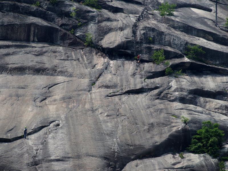 "P4 Belay:End of P4" - The belayer is using the lower belay point (old pin + good gear) thus allowing the leader to also get good gear (Med.- Large Cam, just above belayer) before the run-out slab. If you belay 10-15 ft higher it's off small wires and TCU's. Leader has just finshed P5 and reached dbl bolt anchor below the headwall.