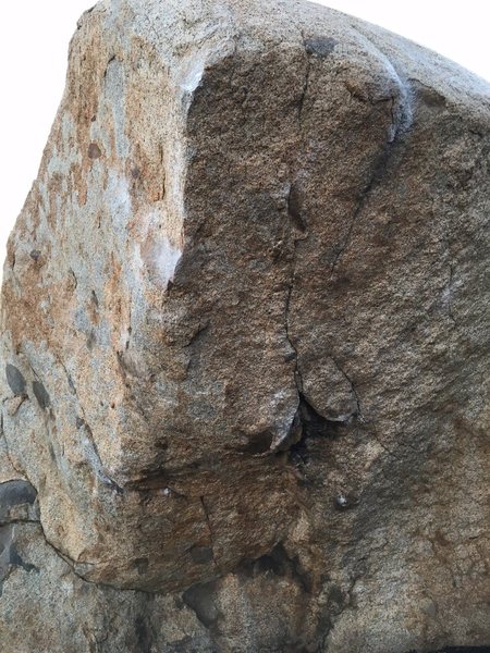 Start both hands around same height (right is at bottom of upside down V at base of crack down center of face). Work left hand up arete to razor sharp edge. Used crappy right heel to get crimp out right, befor big move to top of right arete. Come into flaring crack up top and mantle with difficulty.