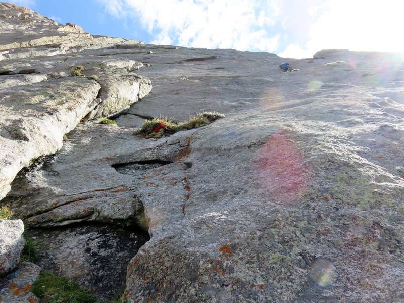 The third pitch starts with a tricky slabby traverse right into a scoop. In this photo, the climber is in the scoop. According to the Kelsey topo, the standard belay would be at the ledge to the left of the scoop, which makes the traverse slightly down and right from the belay. But it is also possible the belay might be lower and that the traverse is more up and right. The traverse seemed harder than 5.6, partly because the leader faces a swing back into the corner. It is possible to set a cam high after the traverse to prevent the follower from facing too large of a swing. After the tricky traverse to the scoop, the pitch finishes easily up broken rock.