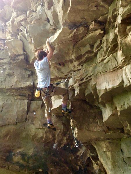 On the bottom start of the roof. There's no need to have a belay on the ledge below the roof, you can easily scramble up past the first bolt to the ledge then stick clip the first bolt.