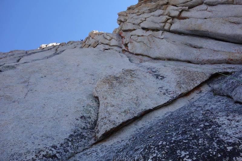 Alternate start to the crest--good for skipping a party that might be slowly pitching out the first pitches. Maybe 5.8+? Follow the left facing corner past bail slings. When the corner gets too steep, tension traverse a few feet left (C1) up to a steep but easy unprotectable runnel (PG). Continue up a full 60m rope length and belay ontop a buttress leading into the true crest. Another 30ft 5.5 pitch up the buttress joins the crest.