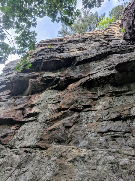 Starts in the middle of the wall, moves up to 1st roof and traverses left. Punch up and over the roof to find easier climbing to the shared anchors.