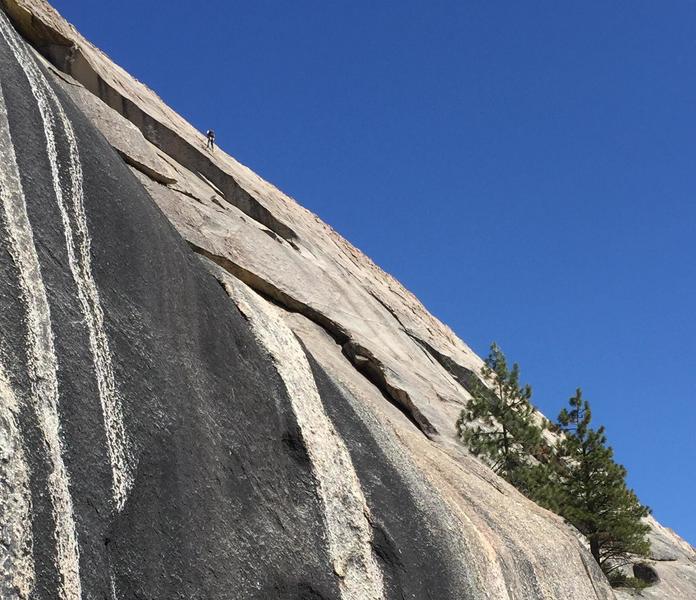 Starting ledge is right of 2 pines (lower right). P2 dihedrail is shadowed upper left. Dihedral exit is where dark and light rock meet near upper left corner. Climber is on Crossing the Milly Way.