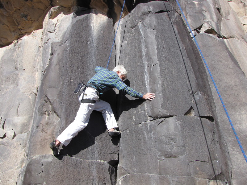 Moment of Inertia climbs the left of two similar dihedrals. The dihedral to the right of the climber is a wholly separate climb, "Obsidian Corner". Chuck Calef is beginning the lower crux sequence which involves long reaches to sloping glass.