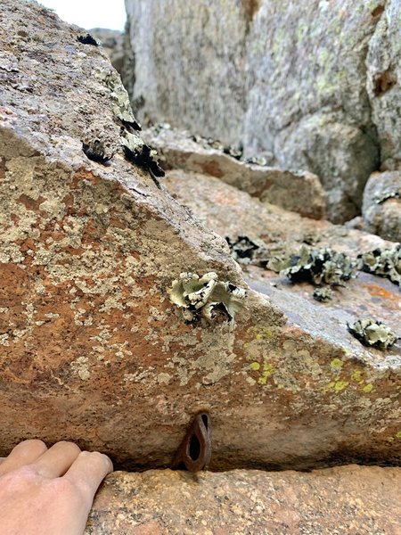 Piton on North Face hand cracks, about 15 feet below and right (north) of the rap station.