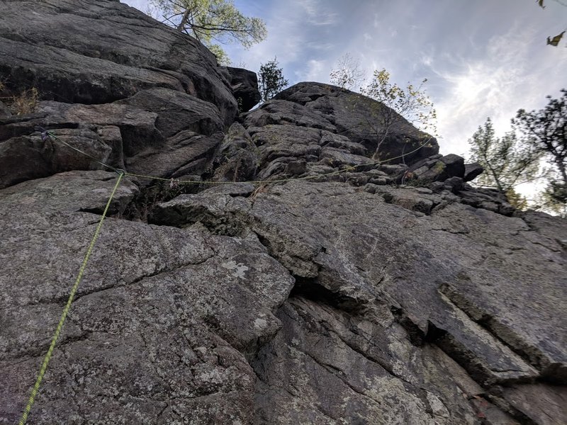 The rope shows the route.  Climb to the end of the double-crack system and continue past the birch tree. Use the short crack to pull the mini roof/bulge at the right side of the upper face (above the cave).  Climb the featured arete to the top.