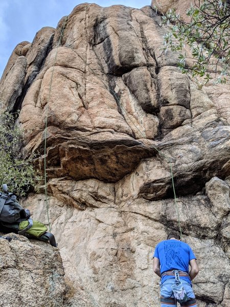 Climber is tying in, route angles to the left after first bolt