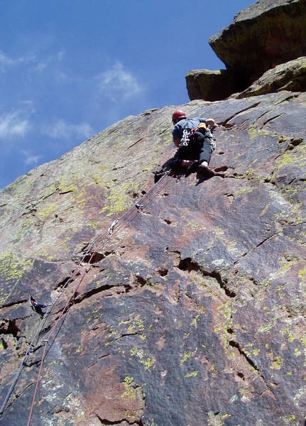 Luke is placing gear in a good crack that isn't very visible fom the ground and continues from where the main crack ends.