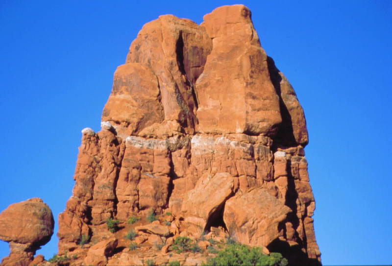 This is a picture of the northeast face with the top of balanced rock on the lower left. The climb starts left of the two big boulders and continues up the center of the formation as seen in this photo. Pitch one ends just on top of the white horizontal band, and yes, the belay stance is obvious currently. If I remember correctly, there is one bolt and a slung chockstone. Continue straight up and then into the chimney that is hidden from view.