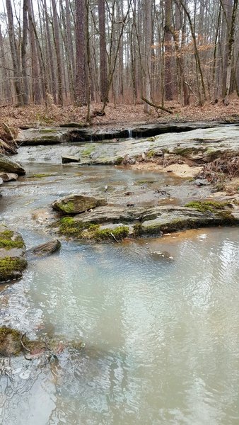 What mineral is causing the cloudy white appearance of the streams seen on this trail?