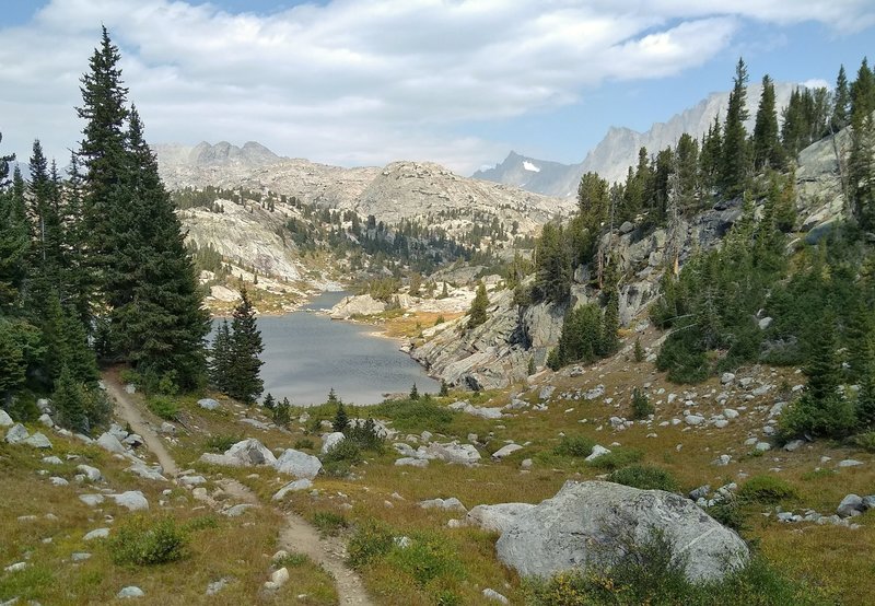 A picturesque small lake with the high peaks of the Wind Rivers in the distance, is seen looking north along the CDT.
