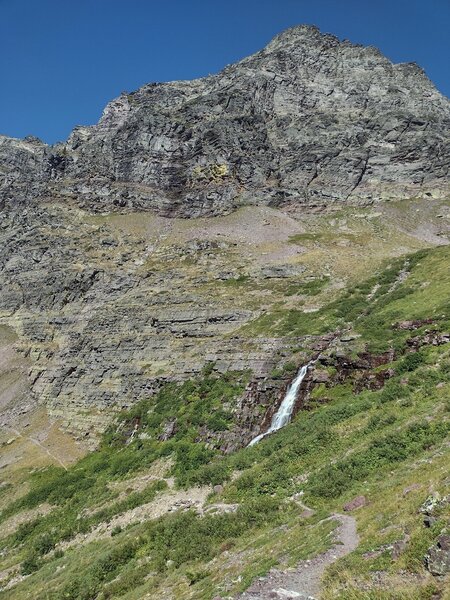 Descending the south side of Gunsight Pass, Gunsight Mountain is high above to the northwest. Headwaters of Lincoln Creek tumble over the waterfall that feeds Lake Ellen Wilson, out of sight below.