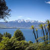 Arawata track features tropical plants and the snow-capped Remarkables mountains behind the crystal blue Lake Wakatipu.